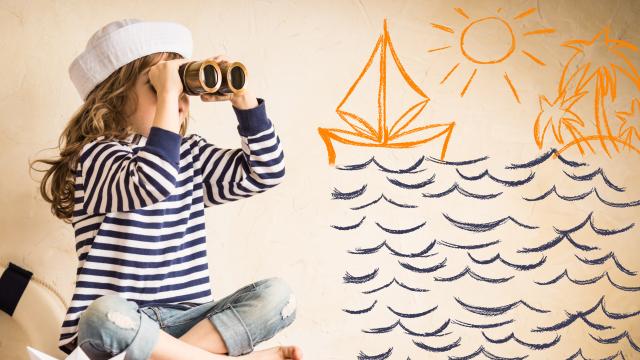 Happy kid playing with toy sailing boat indoors. Travel and adventure concept