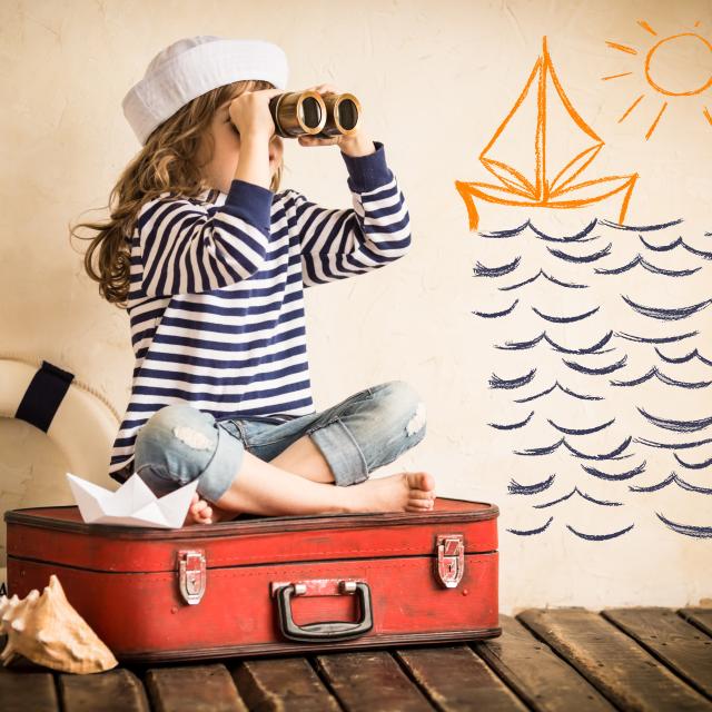 Happy kid playing with toy sailing boat indoors. Travel and adventure concept